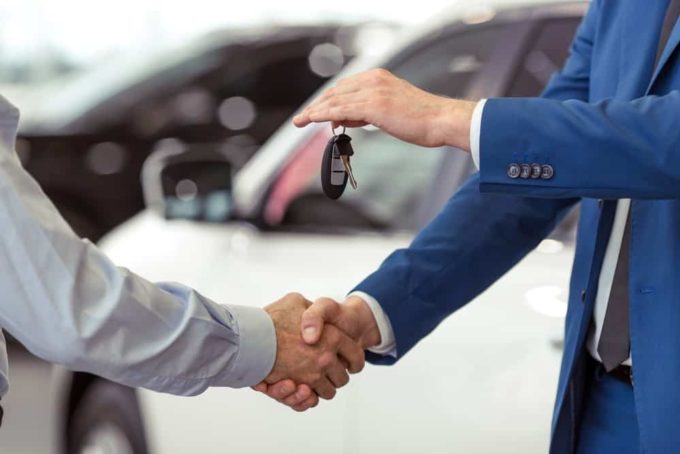 Man in blue suit handing over car keys while shaking hands in front of a white vehicle cash for cars tx – Don't Trade It In