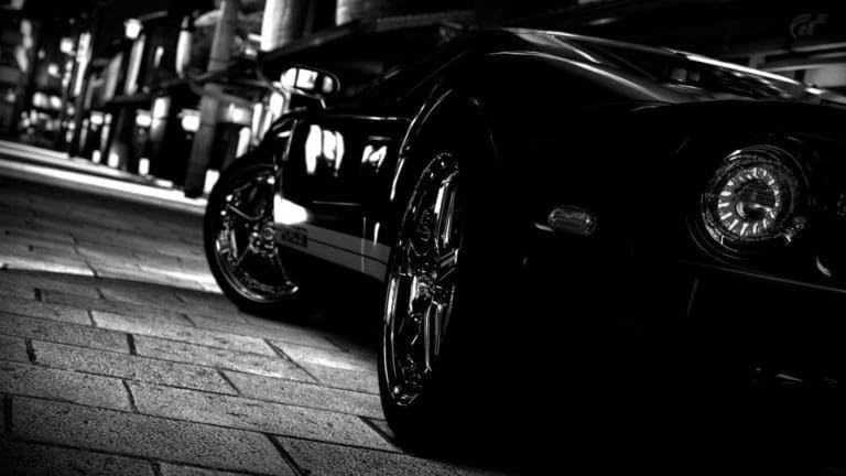 Close-up black and white shot of a sports car parked on a city street at night, focusing on headlight and front wheel Cash for Cars TX - Don't Trade It In