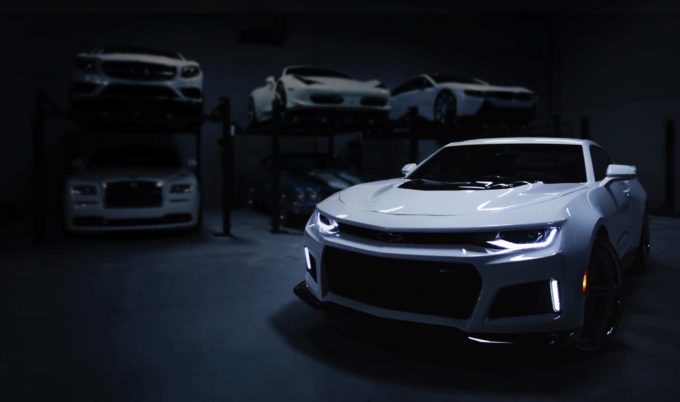 White Chevrolet Camaro parked in a luxury car showroom with high-end vehicles on lifts in the background cash for cars tx – Don't Trade It In
