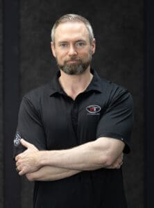 Justin Cole Don't Trade It In Cash for Cars TX representative in black polo shirt, standing with arms crossed - Don't Trade It In